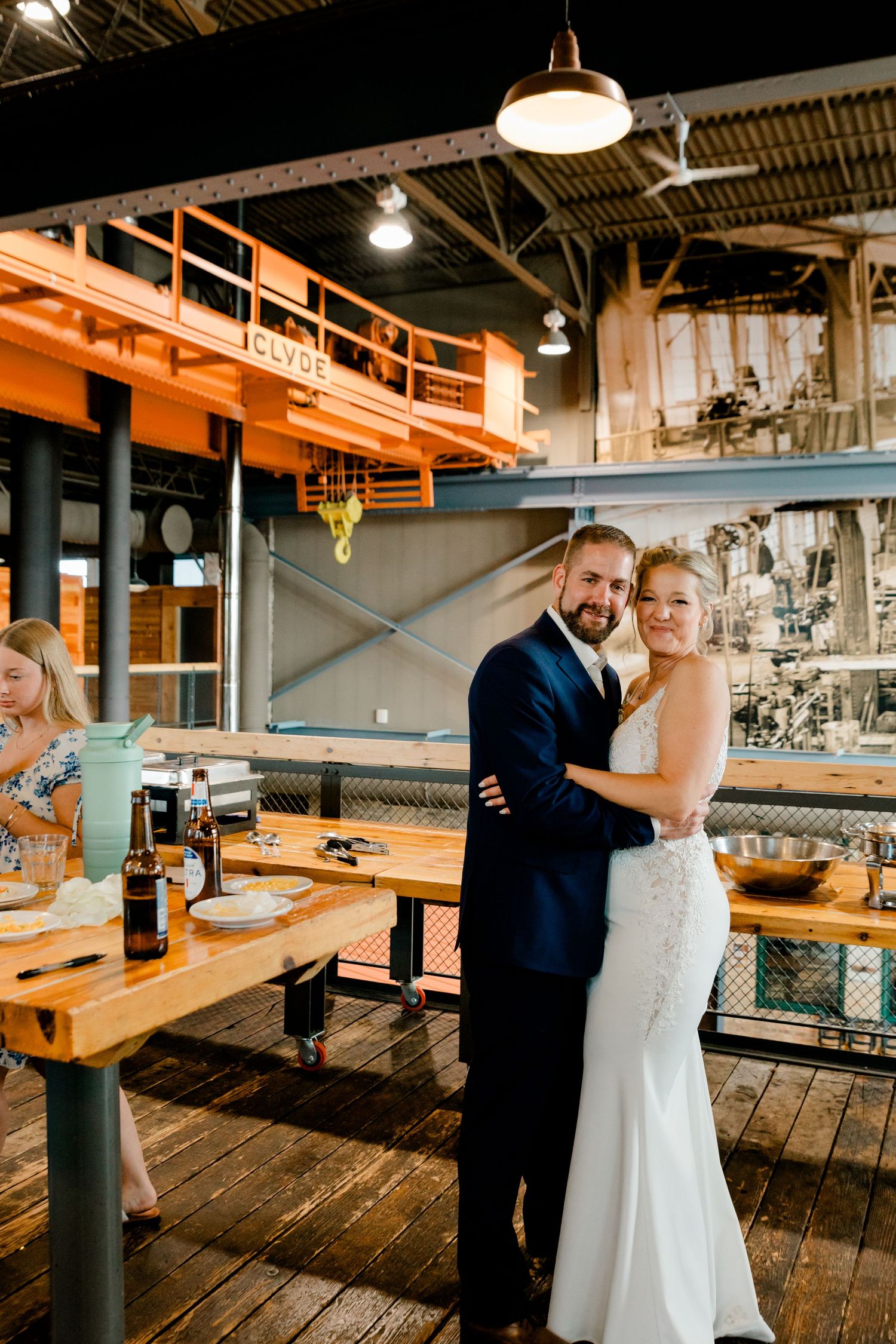 Bride and groom pose together inside an industrial-style wedding venue with orange steel beams.