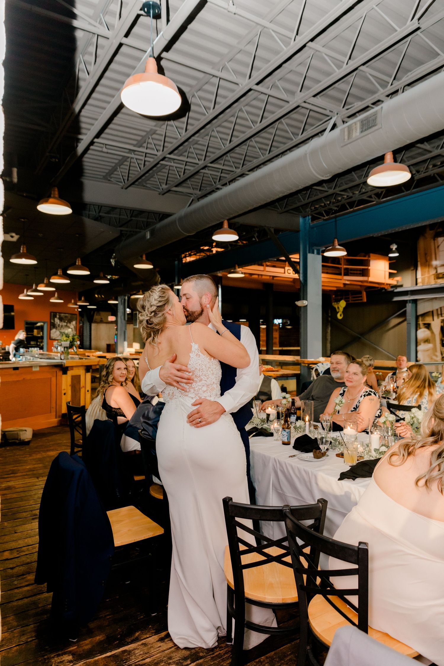 Bride and groom share their first kiss on the dance floor surrounded by seated wedding guests.
