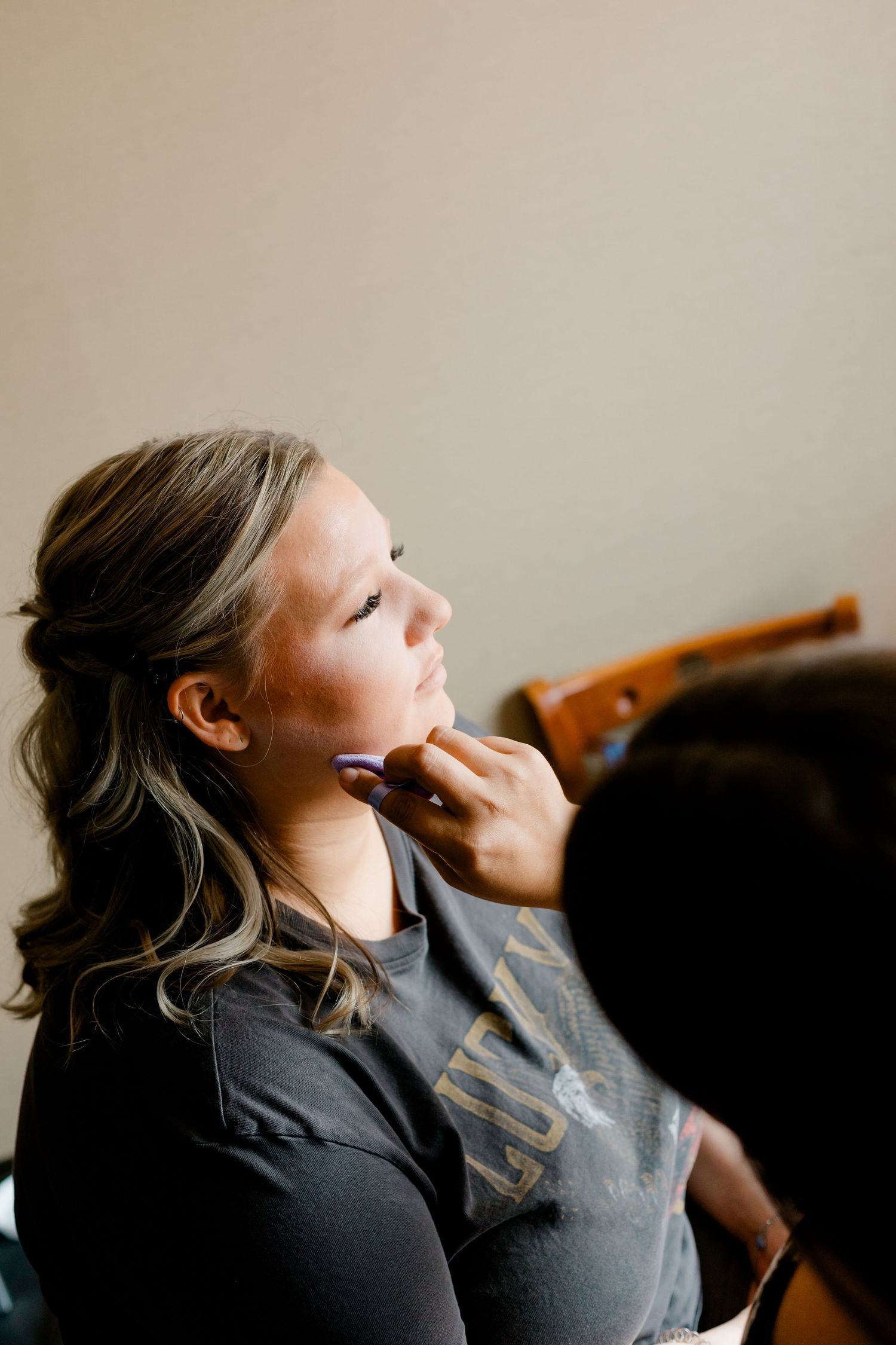 Young girl getting makeup applied by a professional artist, looking upward with a calm expression.
