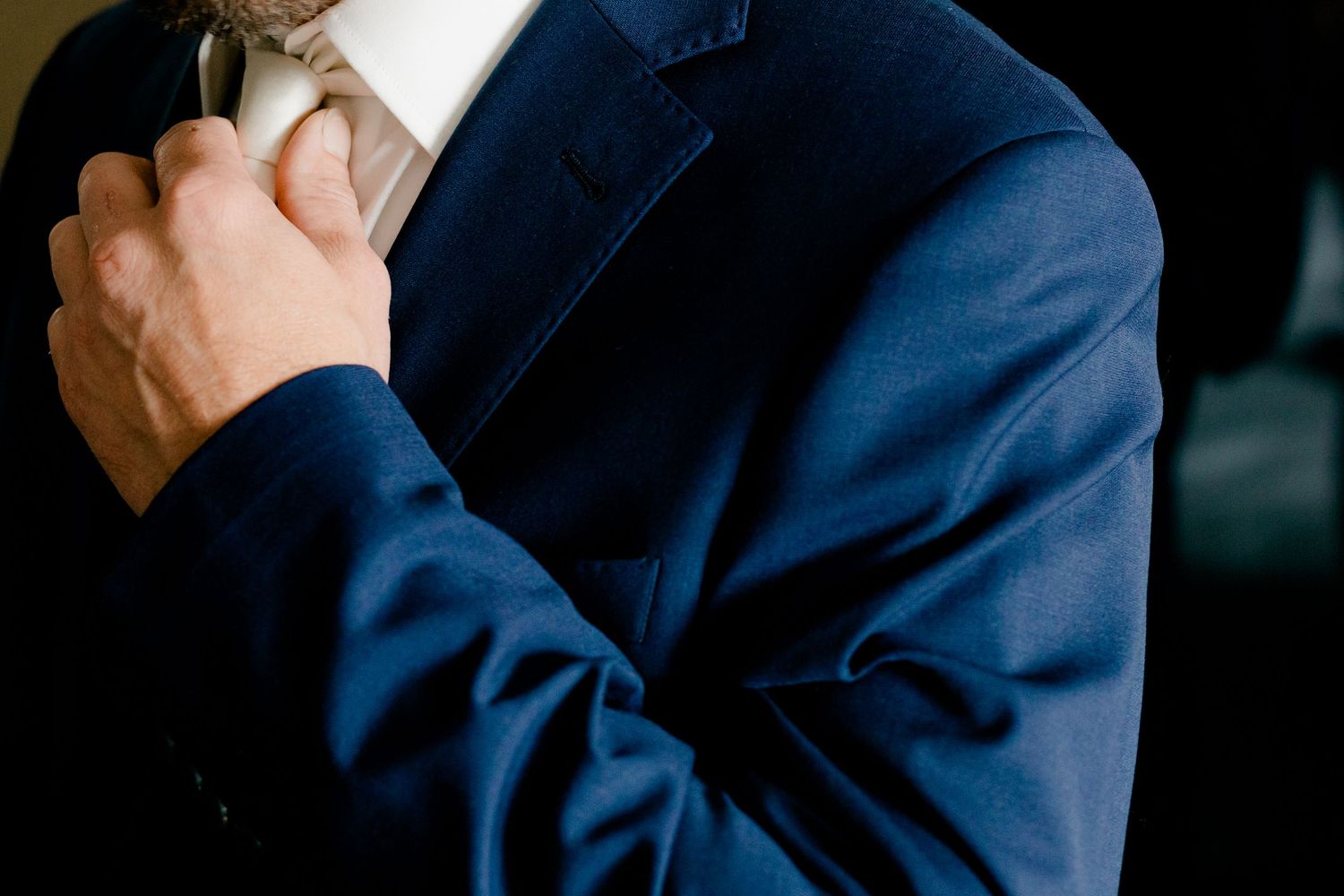 Man in navy blue suit adjusting white tie, close-up professional formal wear photo.