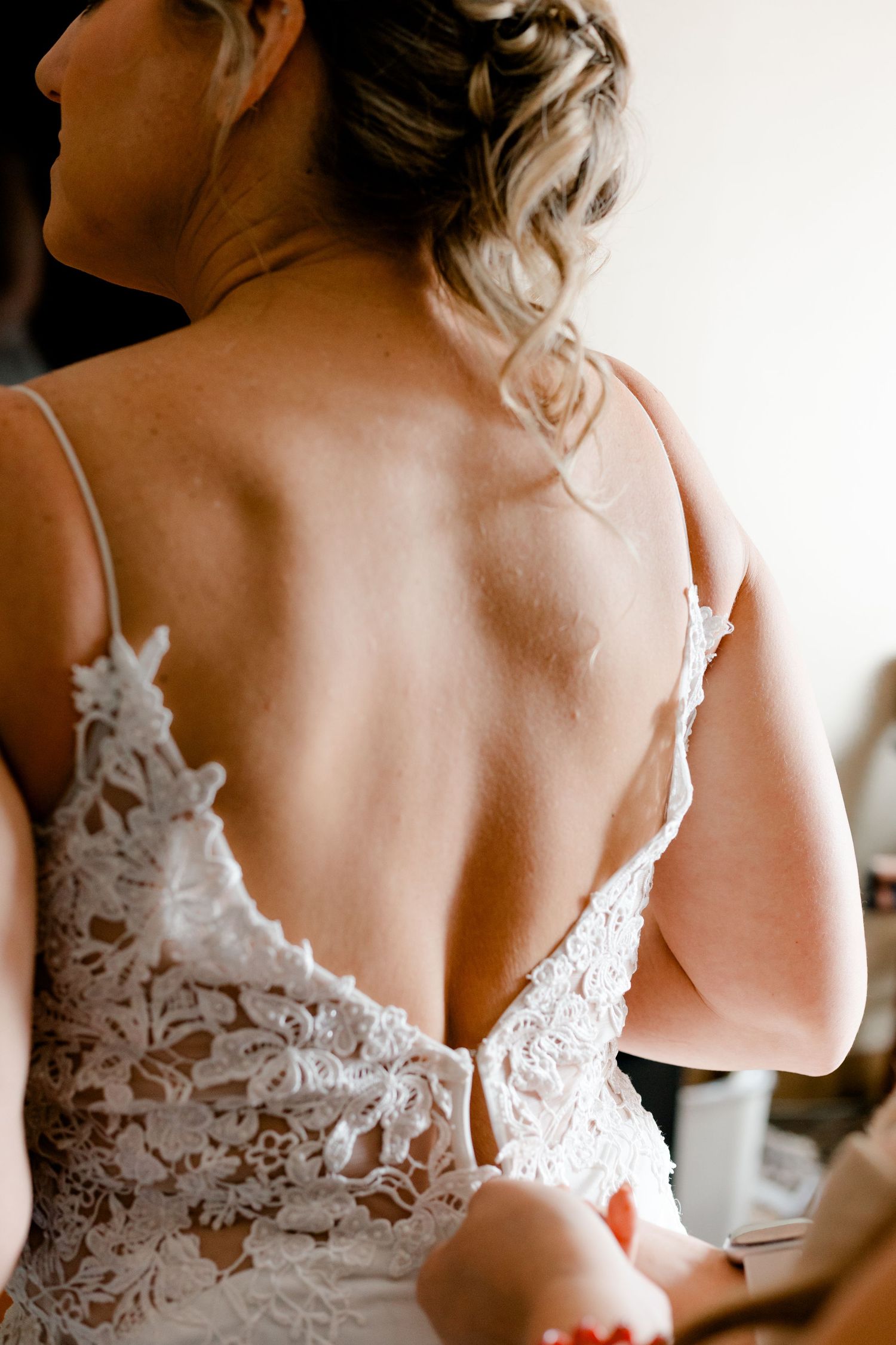 Close-up back view of bride in elegant low-back lace wedding gown with delicate spaghetti straps.