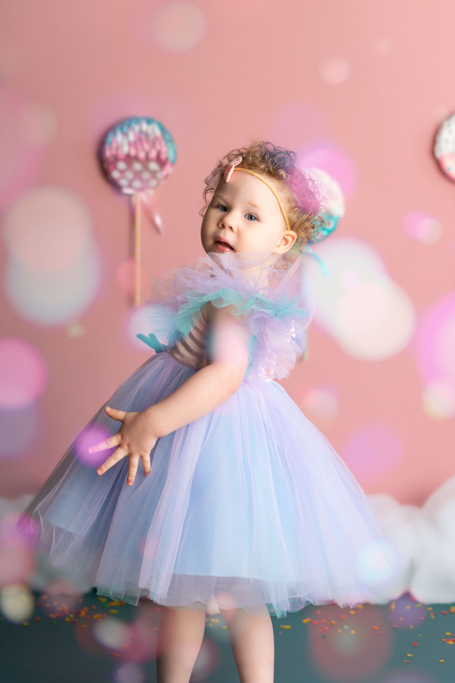 A series of dreamy photos showing a toddler in a blue tulle dress twirling against a pink bokeh background.