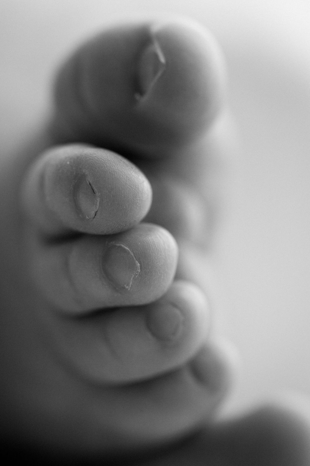 A series of black and white macro photographs showing soft curves and abstract shapes with shallow depth of field, with baby toes.