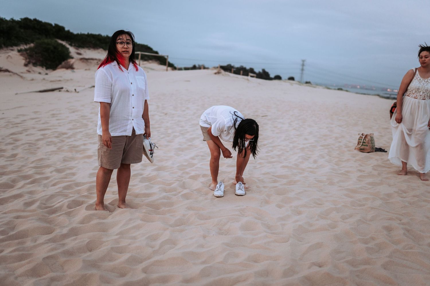 Group of people spending time together on a sandy beach at dusk with hills in the background.