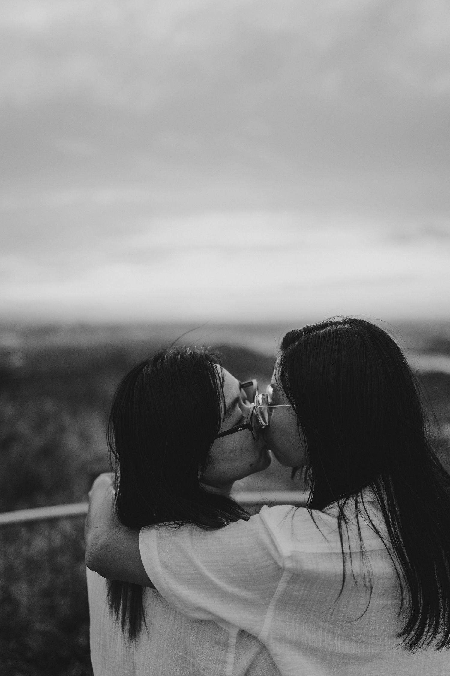 Two people sharing an intimate black and white moment outdoors against a blurred scenic landscape background.