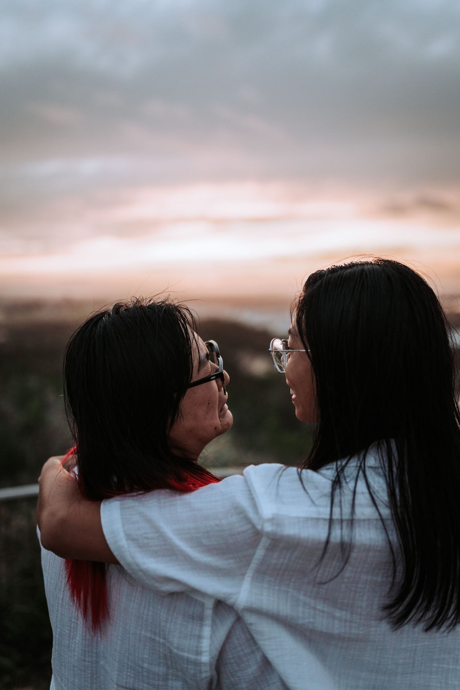 Two people in white shirts share an intimate moment while watching the sunset together against a dusky sky.
