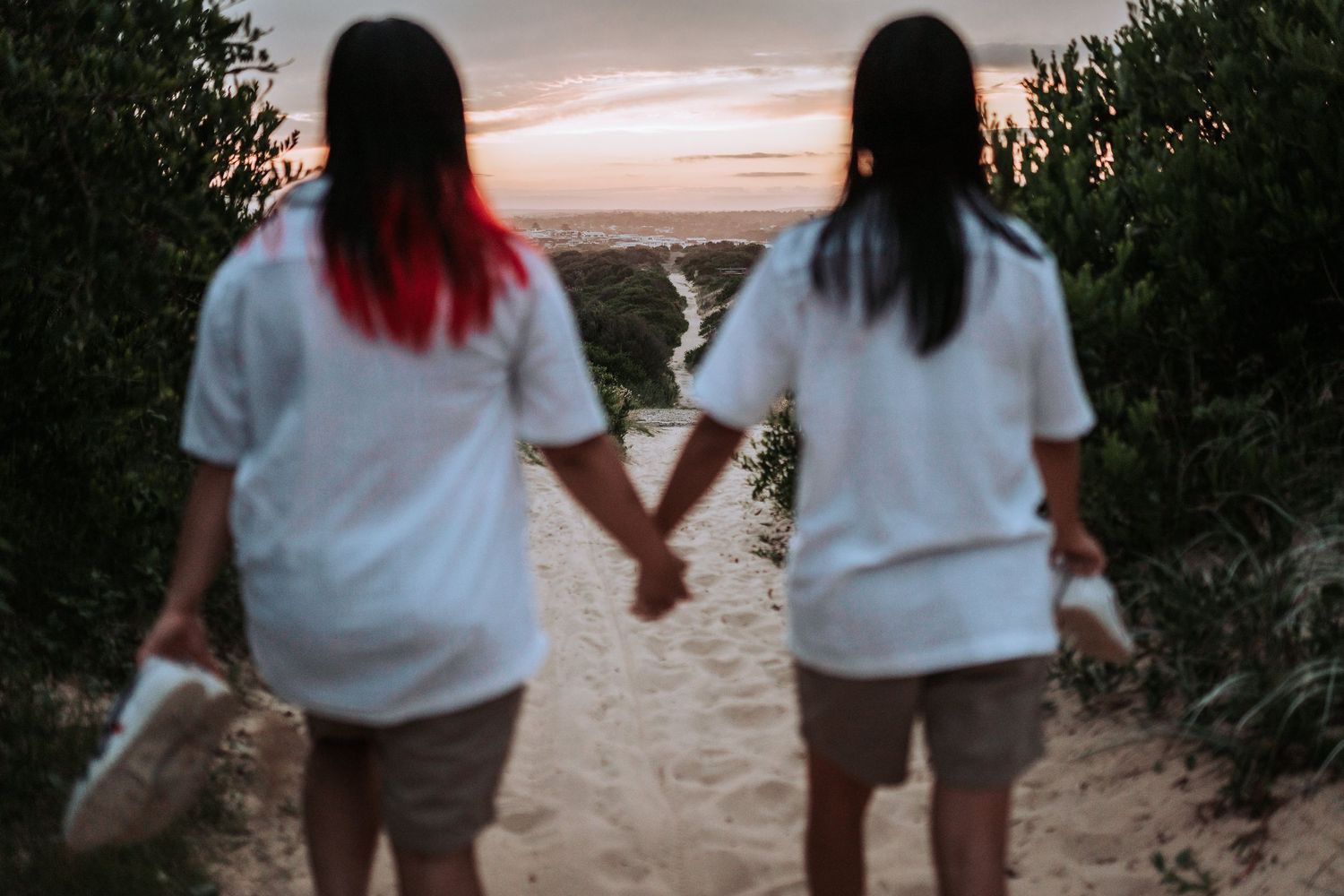 Two people in white shirts holding hands on a sandy path at sunset overlooking a scenic vista.