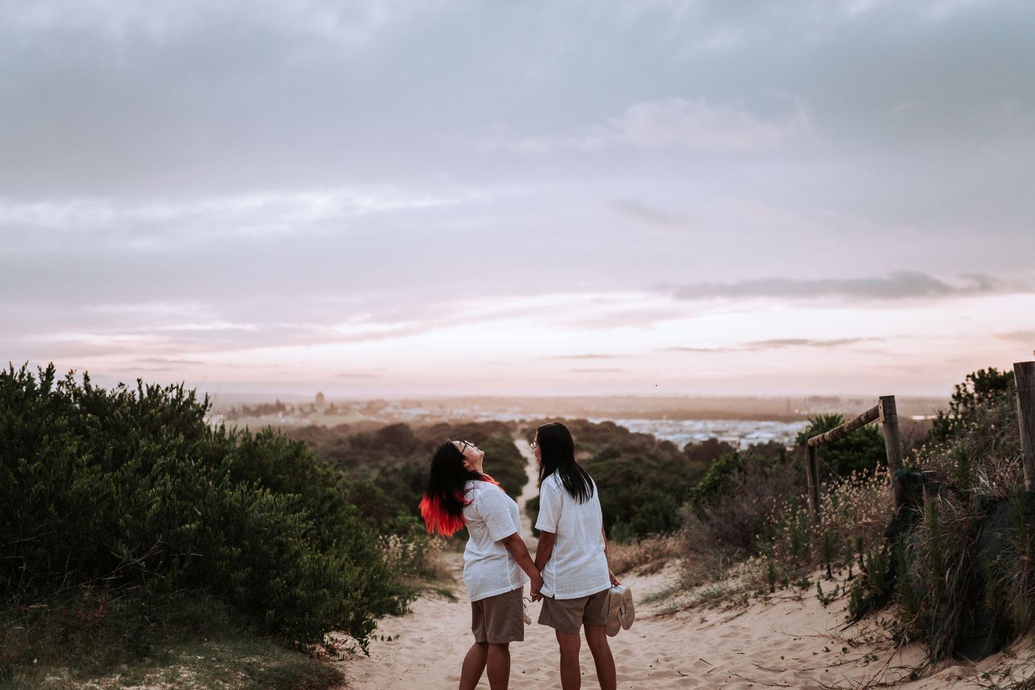 People stand together on a sandy coastal path at sunset overlooking a misty beach landscape.