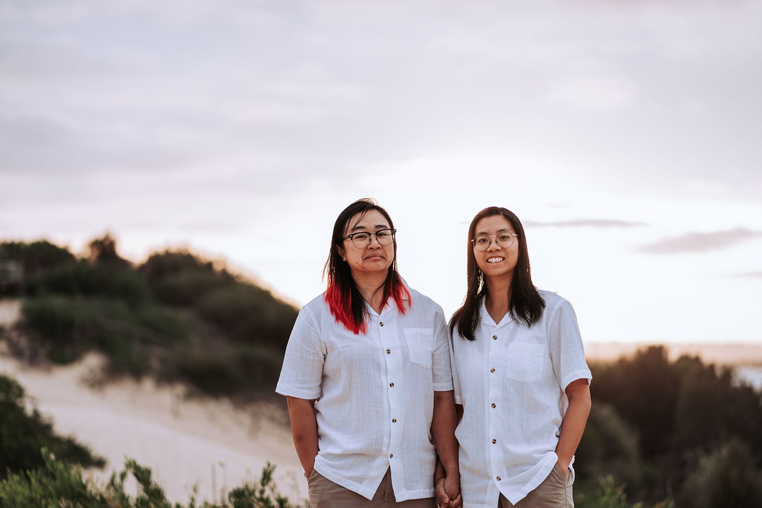 Two people in matching white button-down shirts stand together on a hilltop at sunset.