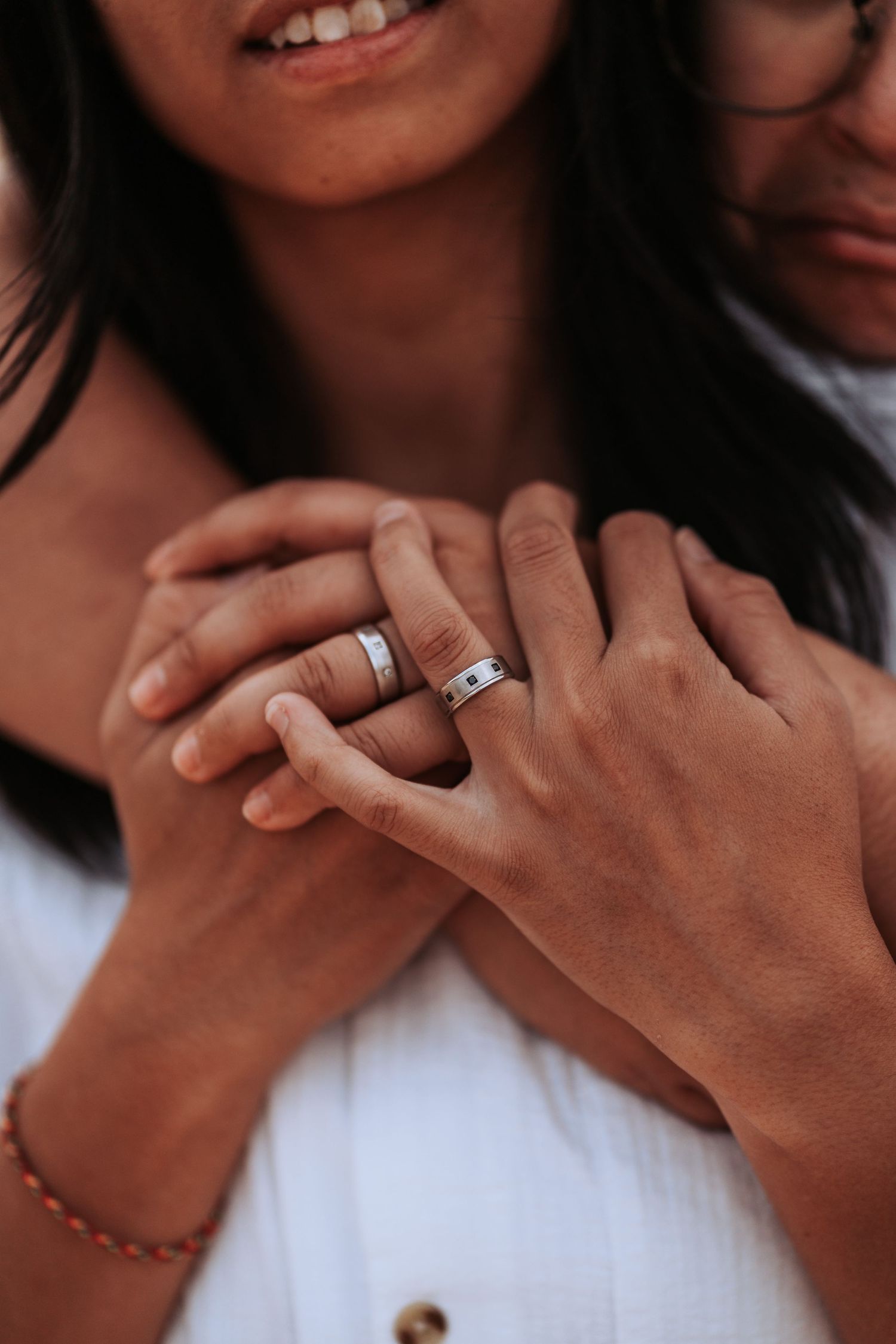 Close up photo showing hands with matching wedding bands and a warm intimate embrace.