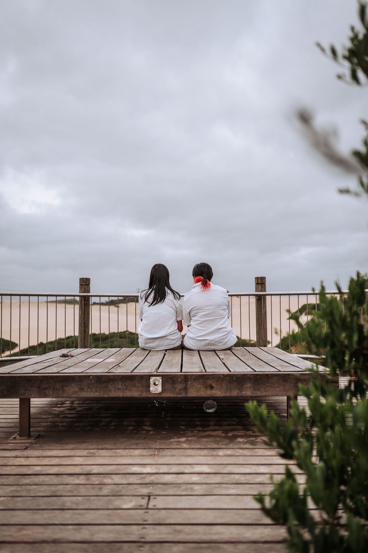 Two people in white shirts sit together on a wooden deck overlooking a cloudy landscape.
