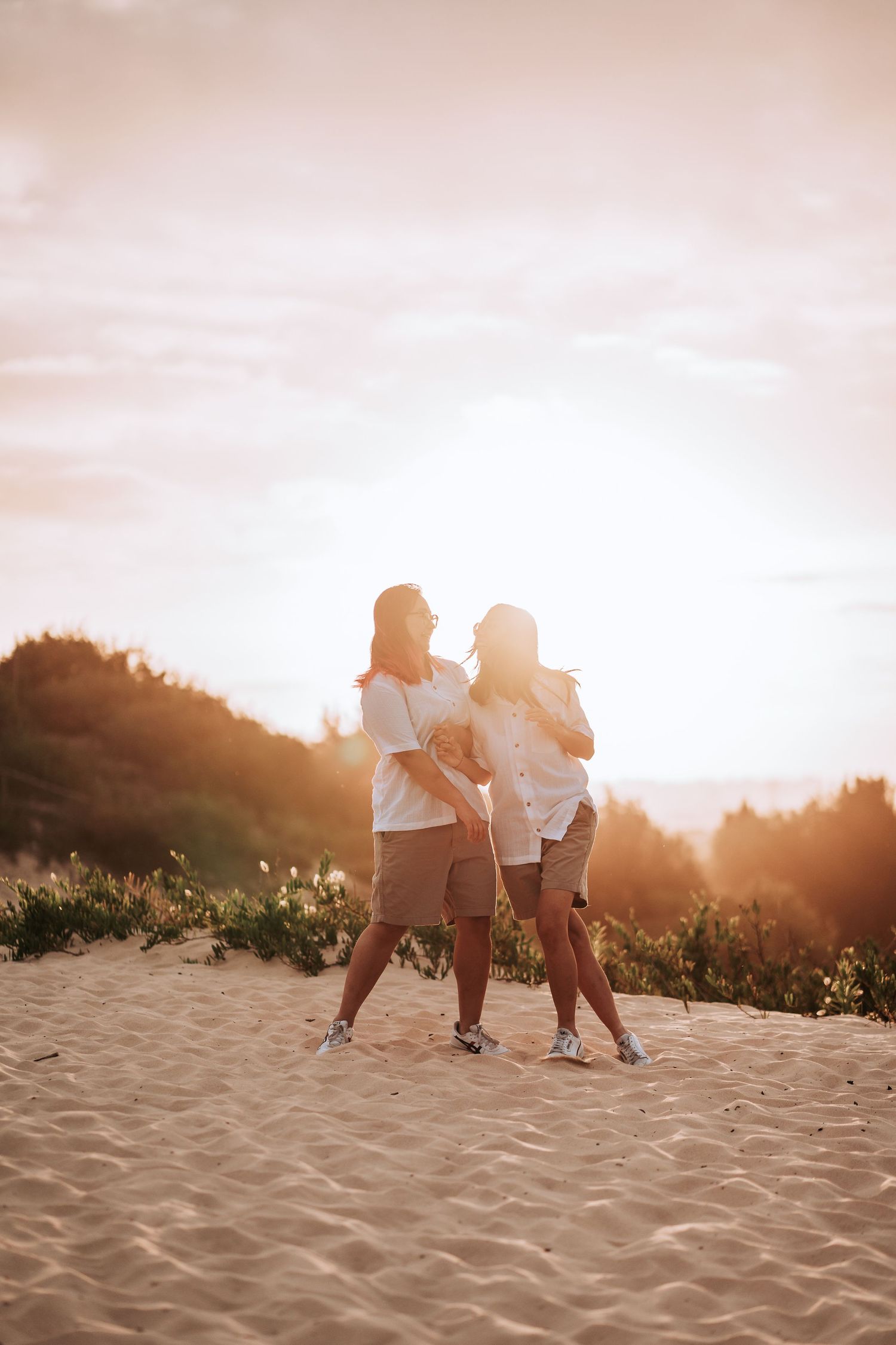 Two silhouetted figures dancing together on sandy beach during golden sunset hour.