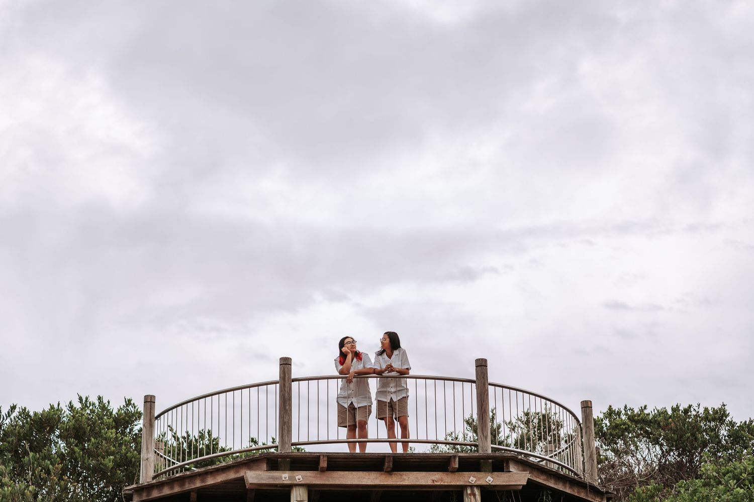 Two people stand together on a circular wooden observation deck against a cloudy sky.