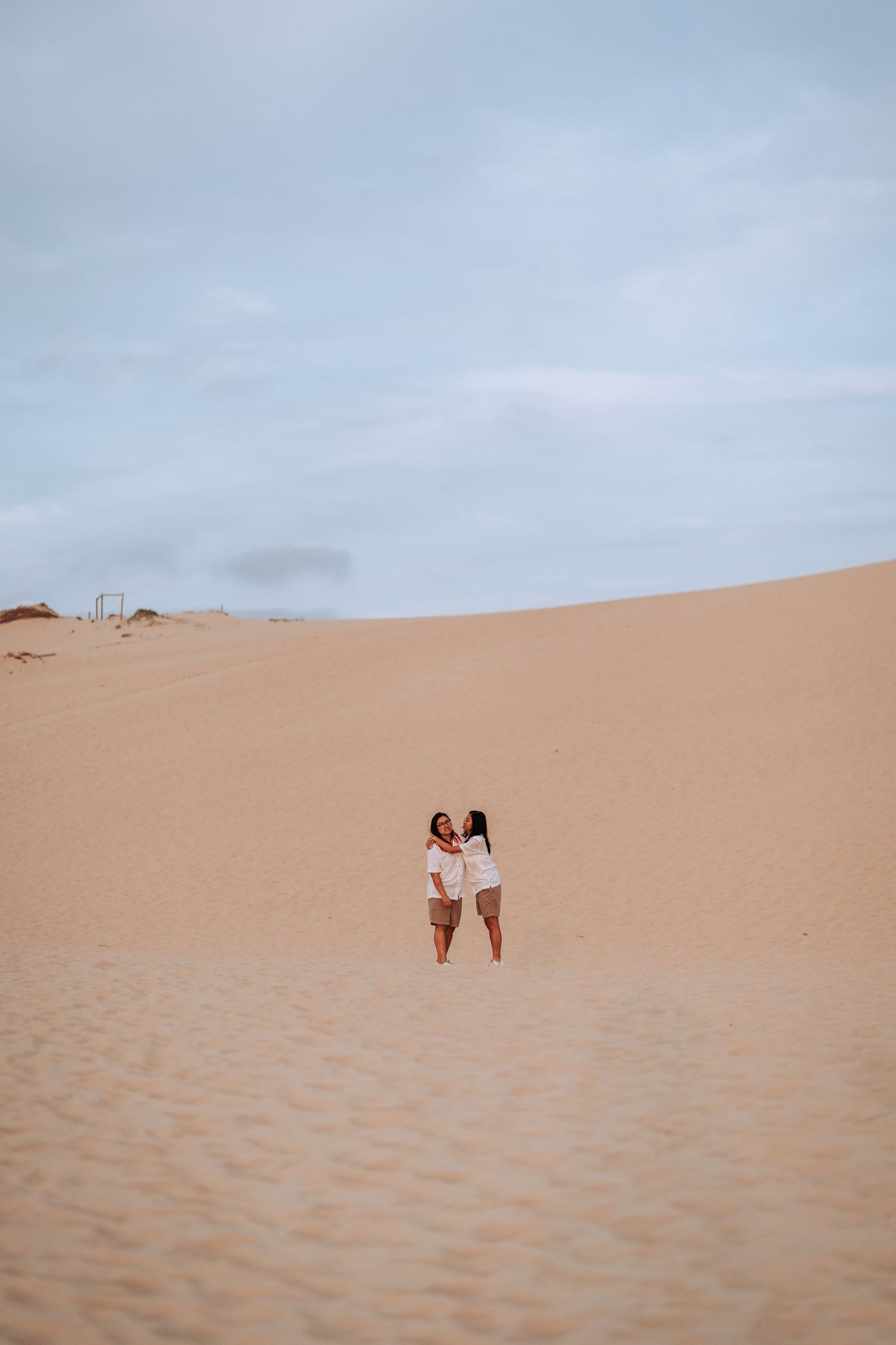 Two people standing together on vast sand dunes with a cloudy sky overhead.