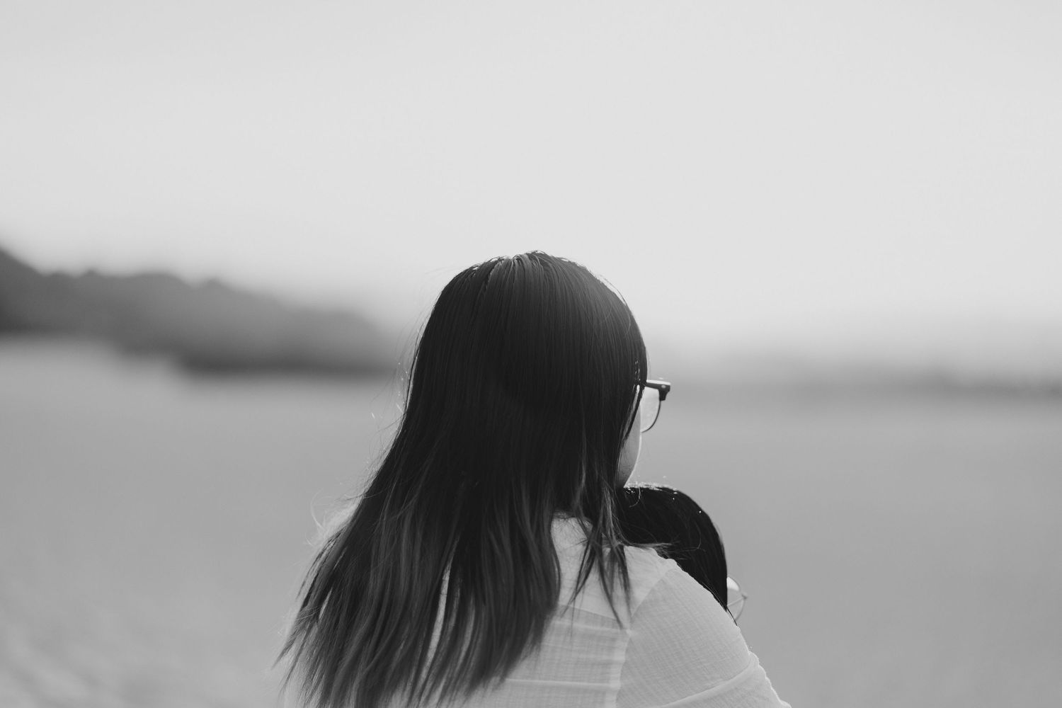 Black and white profile silhouette of a person looking at a blurry landscape view outdoors.