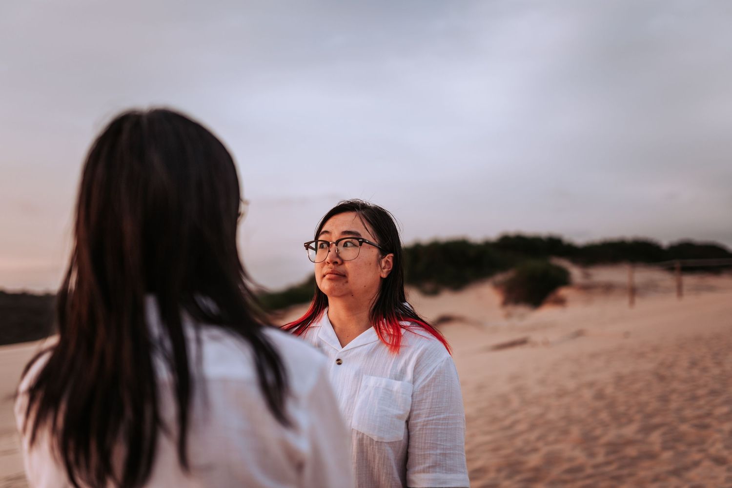 Two people having an emotional conversation on a sandy beach at dusk with cloudy skies in the background.