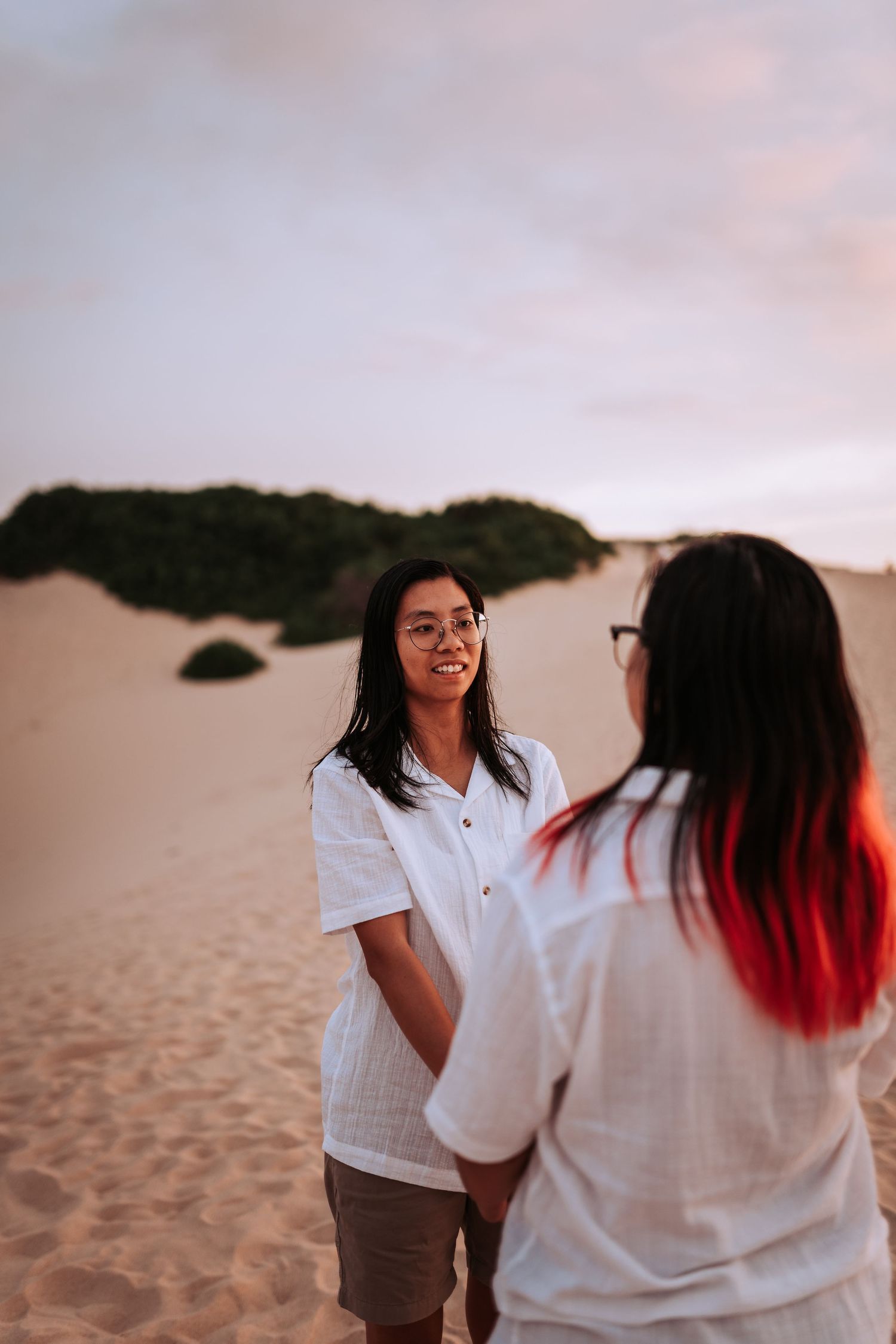 Two people in white shirts share a joyful moment together on a sandy beach during sunset.