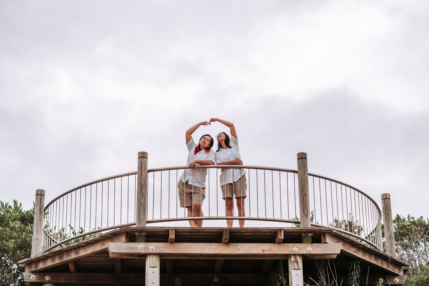 A person stands on a wooden observation deck with curved railings against a cloudy sky.