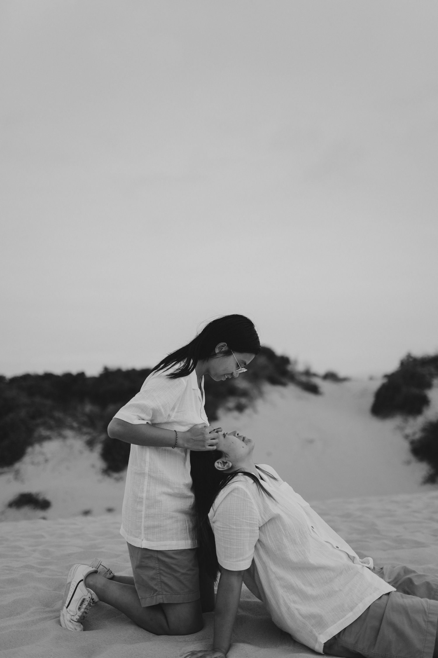 A intimate black and white photo of a couple posed together on sand dunes at sunset.