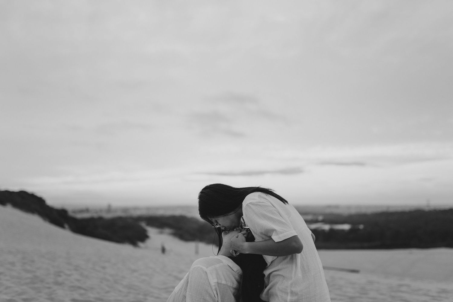 A romantic black and white silhouette of a couple sharing a moment at sunset on a scenic hilltop.