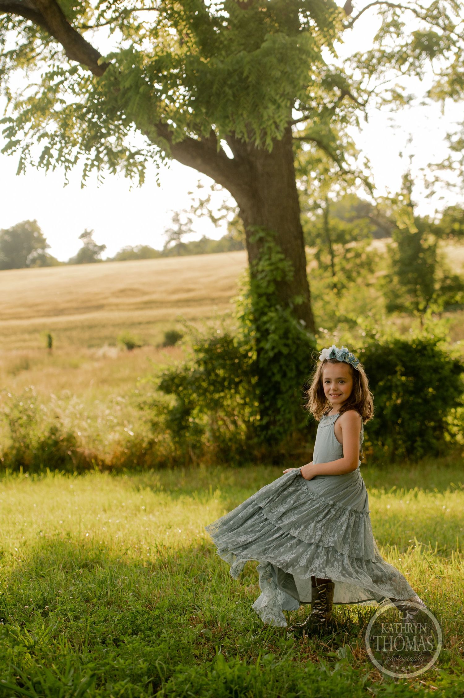 Playful twirl in a sage dress captured during golden hour beneath a sprawling tree.