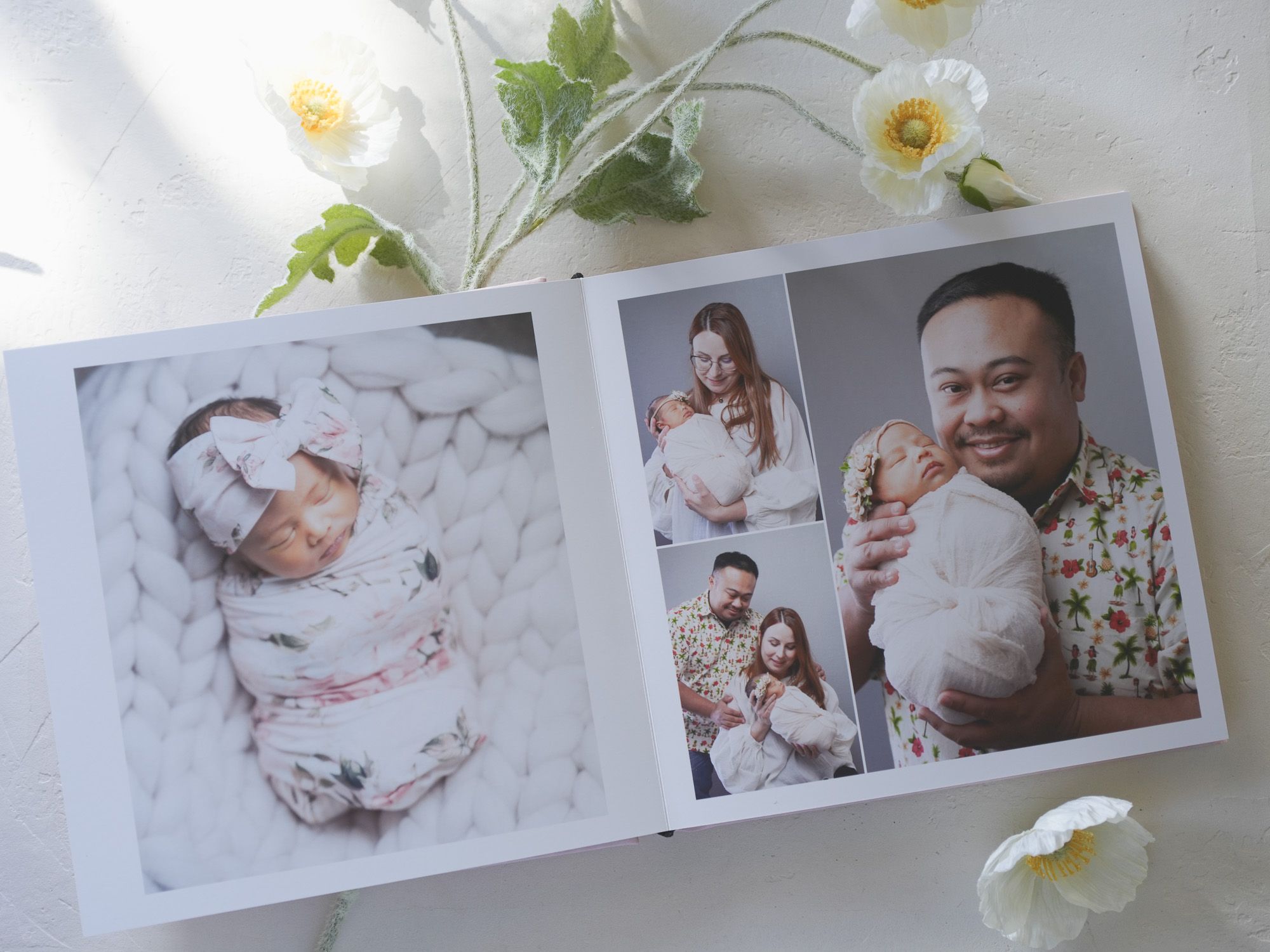Photo album pages displaying newborn and family portraits with white floral decorations.