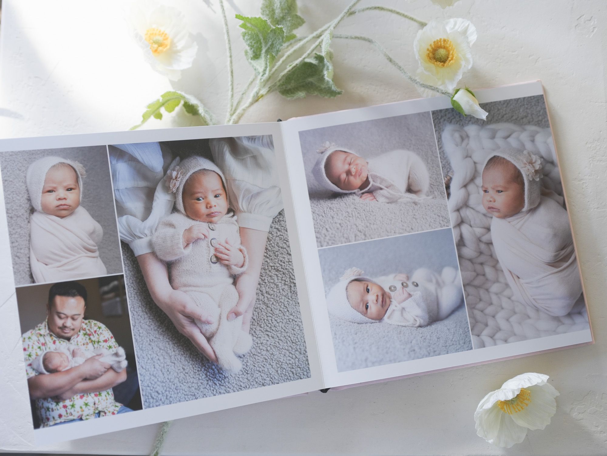 Professional baby photo album page showing sweet newborn portraits in soft neutral tones with white flowers.