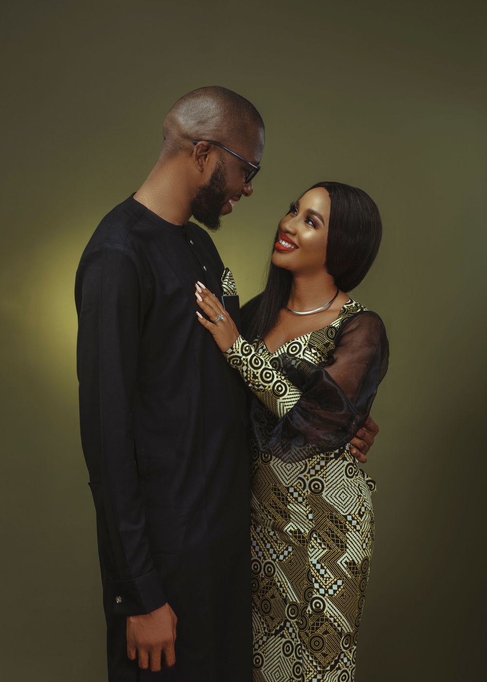 A couple in semi-formal attire share an intimate moment against a dark green background.