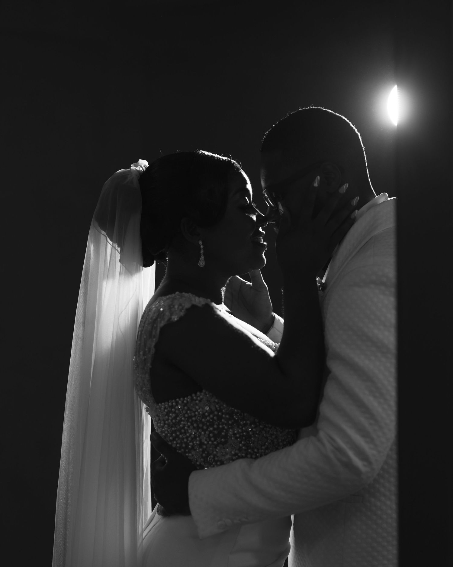 Dramatic black and white portrait of wedding couple in intimate embrace with backlit effect.