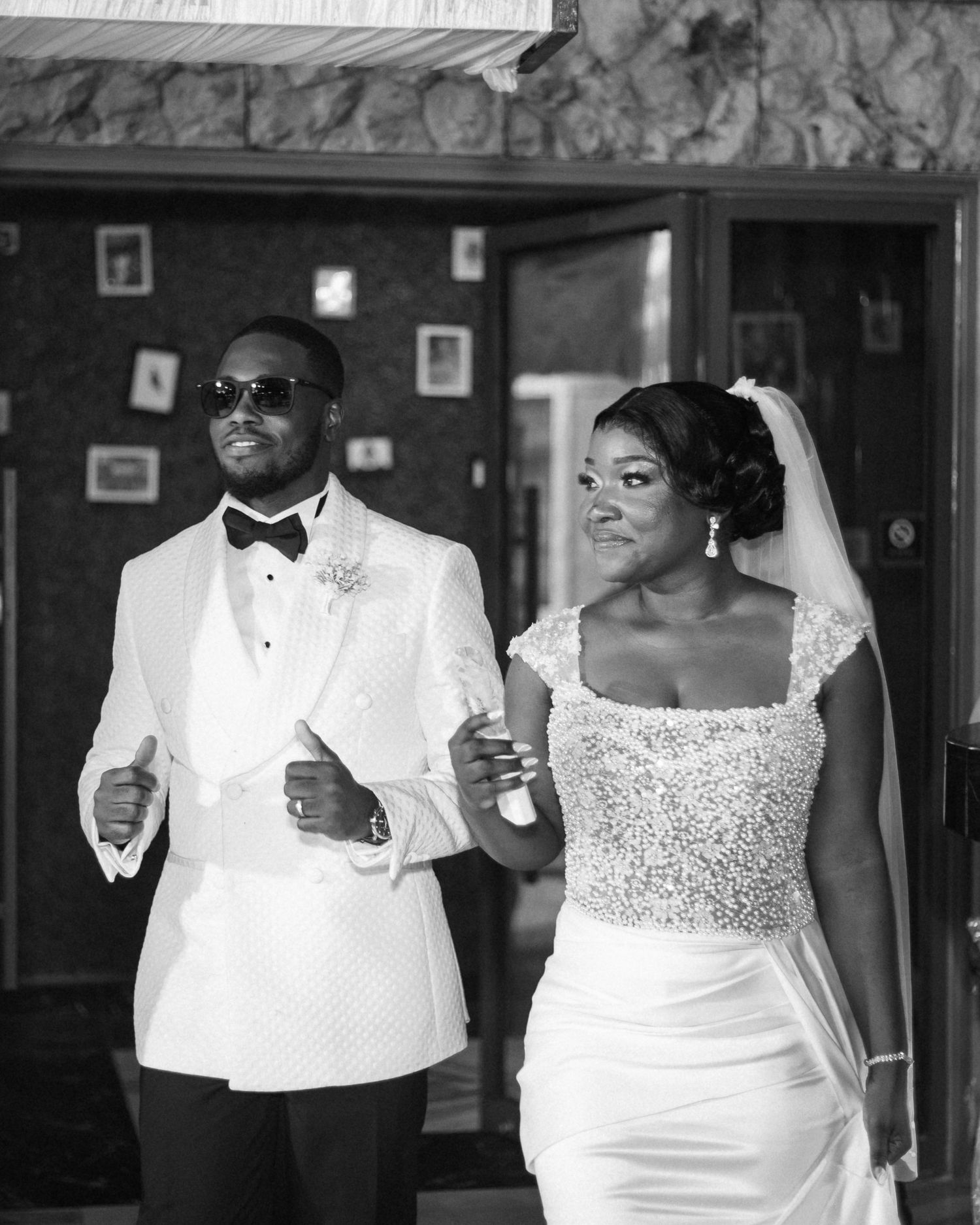 Black and white photo of couple in formal wedding attire walking together with joyful expressions.
