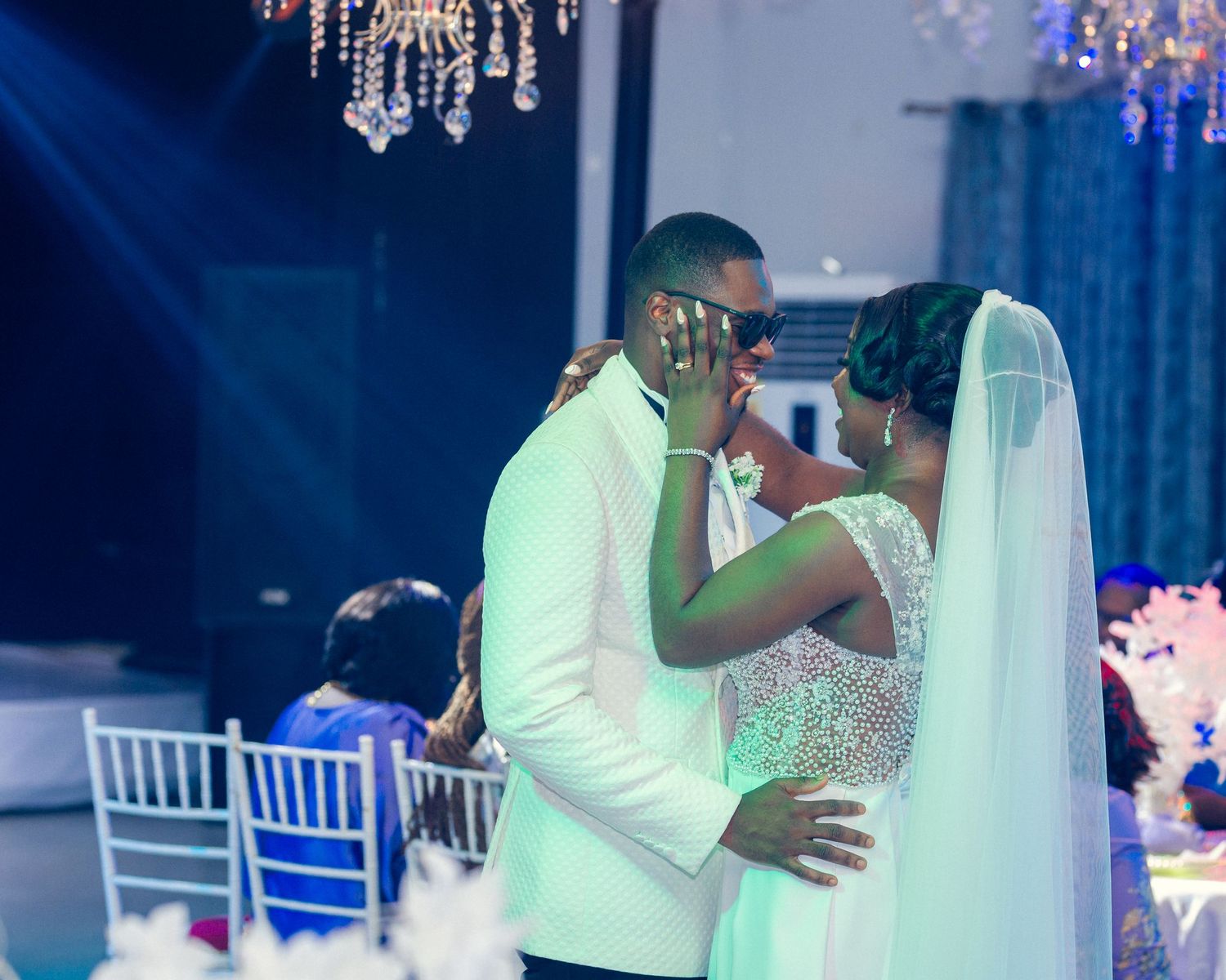 Intimate moment between couple during wedding reception under sparkling chandelier lights.