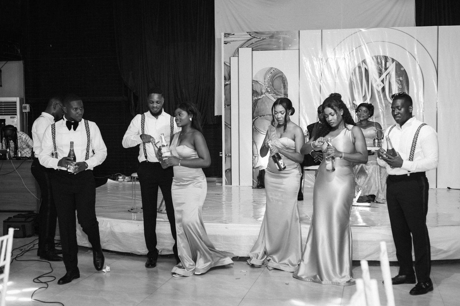 Wedding party in formal attire gathers for candid black and white photo at reception.