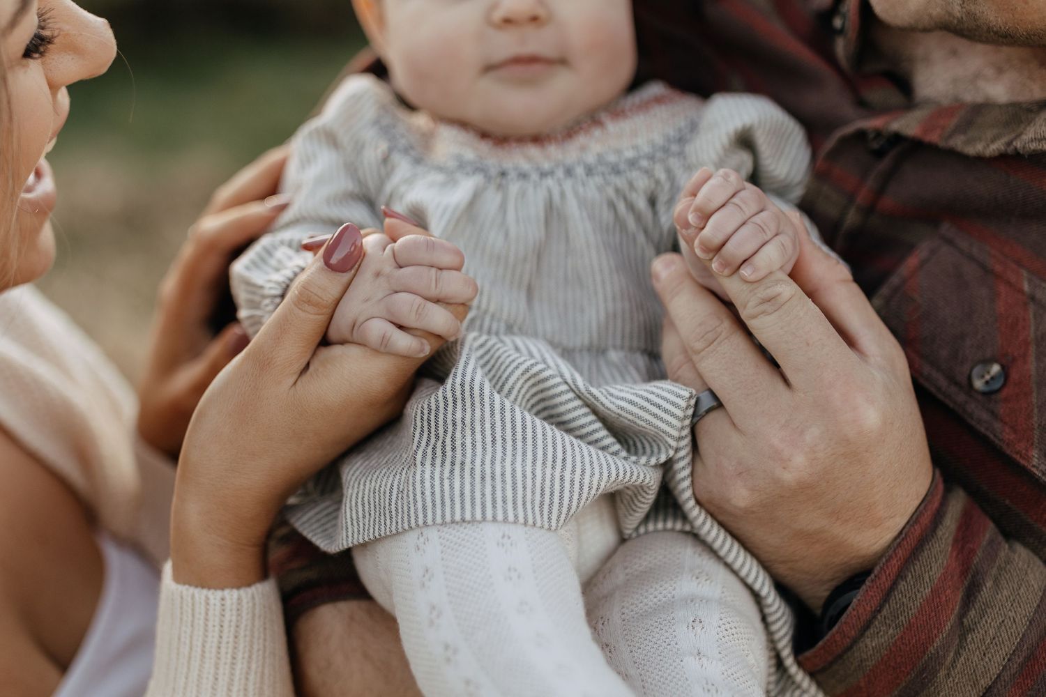 Close-up shot of hands holding a baby wearing a knitted gray outfit.