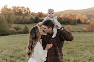 A playful family photo session in a scenic autumn field with rolling hills in the background.