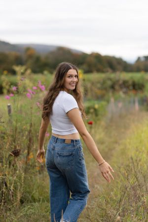 Person wearing a white crop top and blue jeans poses in a field of wildflowers during golden hour.