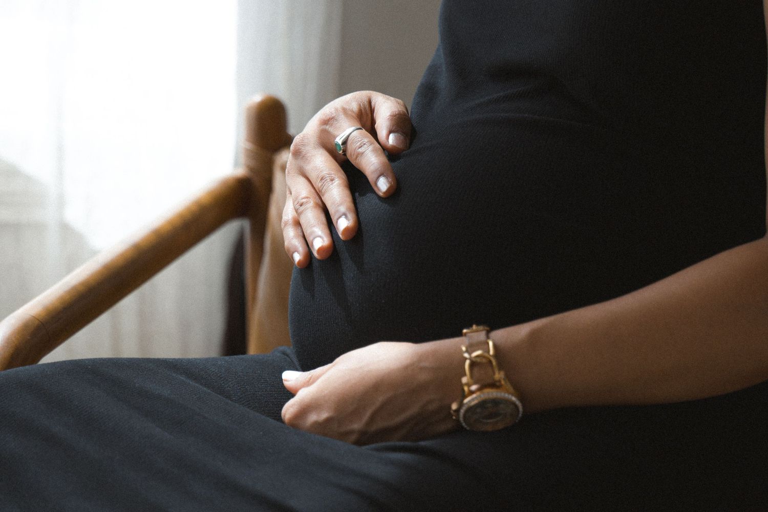 Pregnant woman in black dress touching her belly in natural light during a maternity photosession in Vancouver, BC.