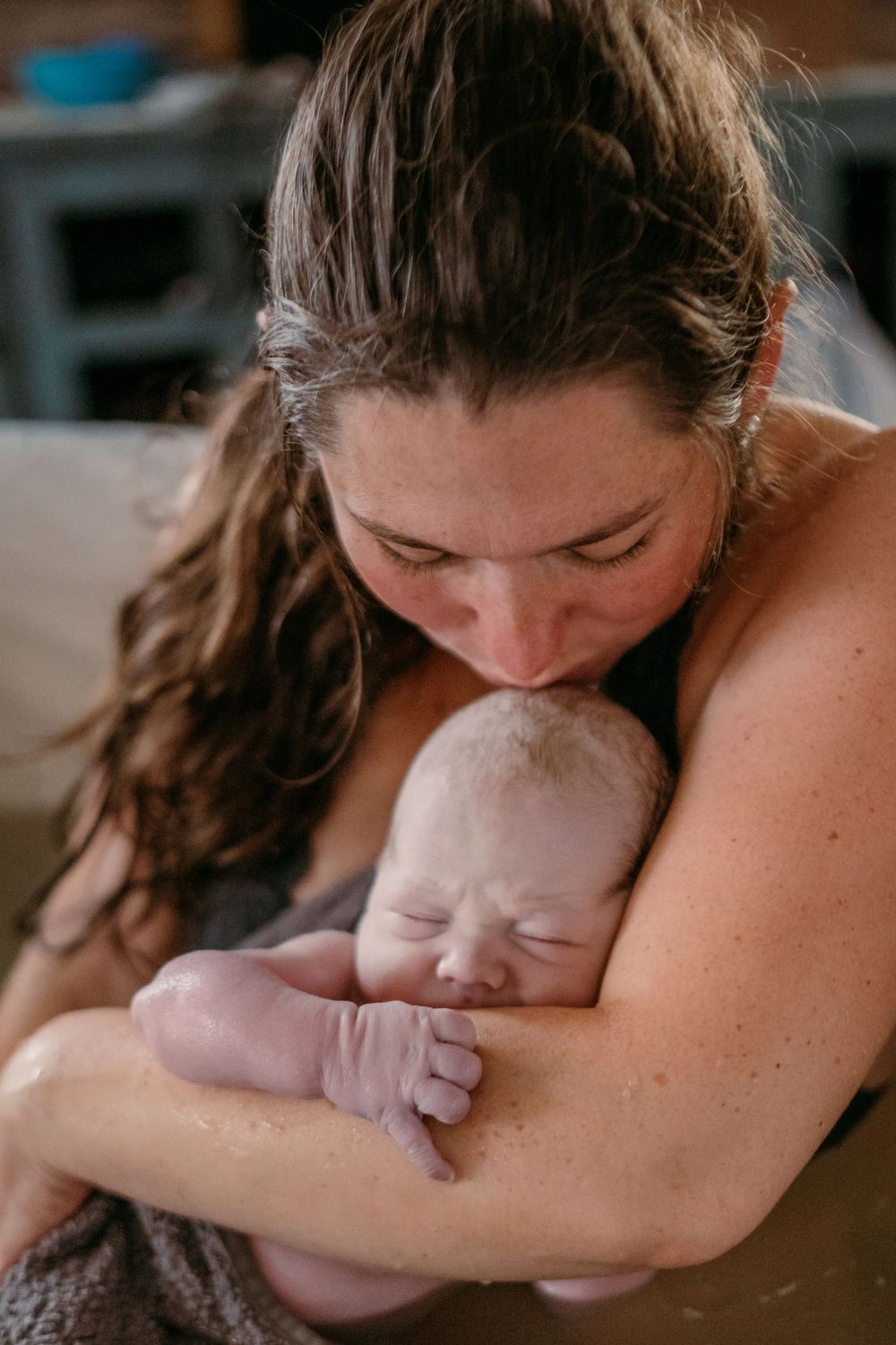 An intimate moment captured as a mother holds and kisses her sleeping newborn baby.