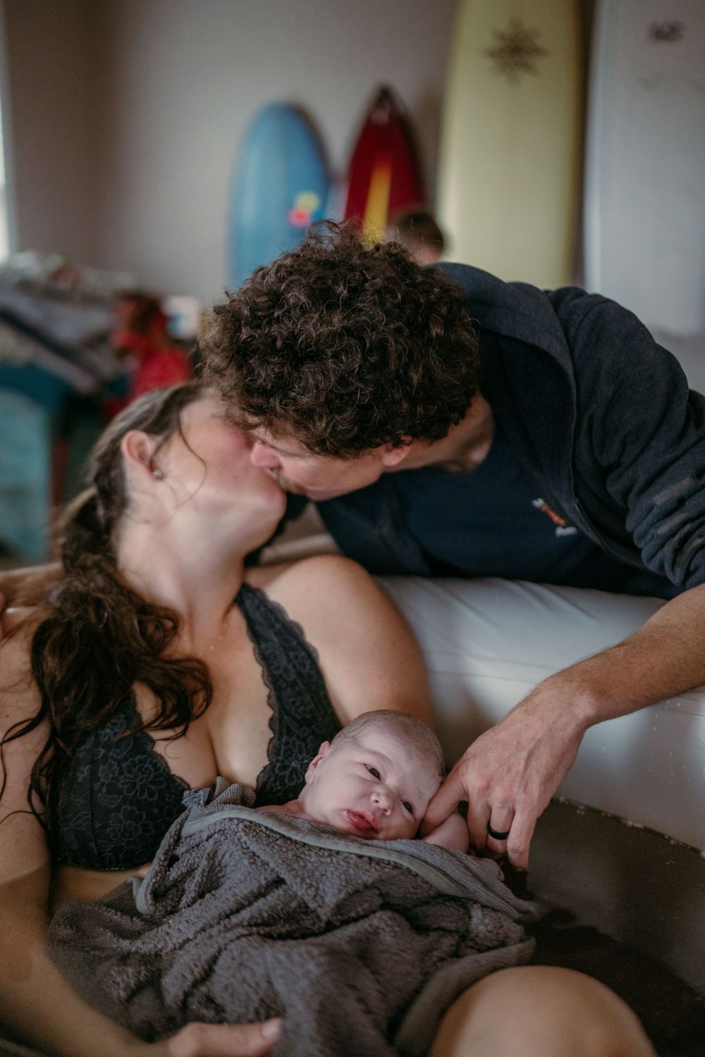 Parents share an intimate moment as their newborn baby rests between them on a cozy bed.