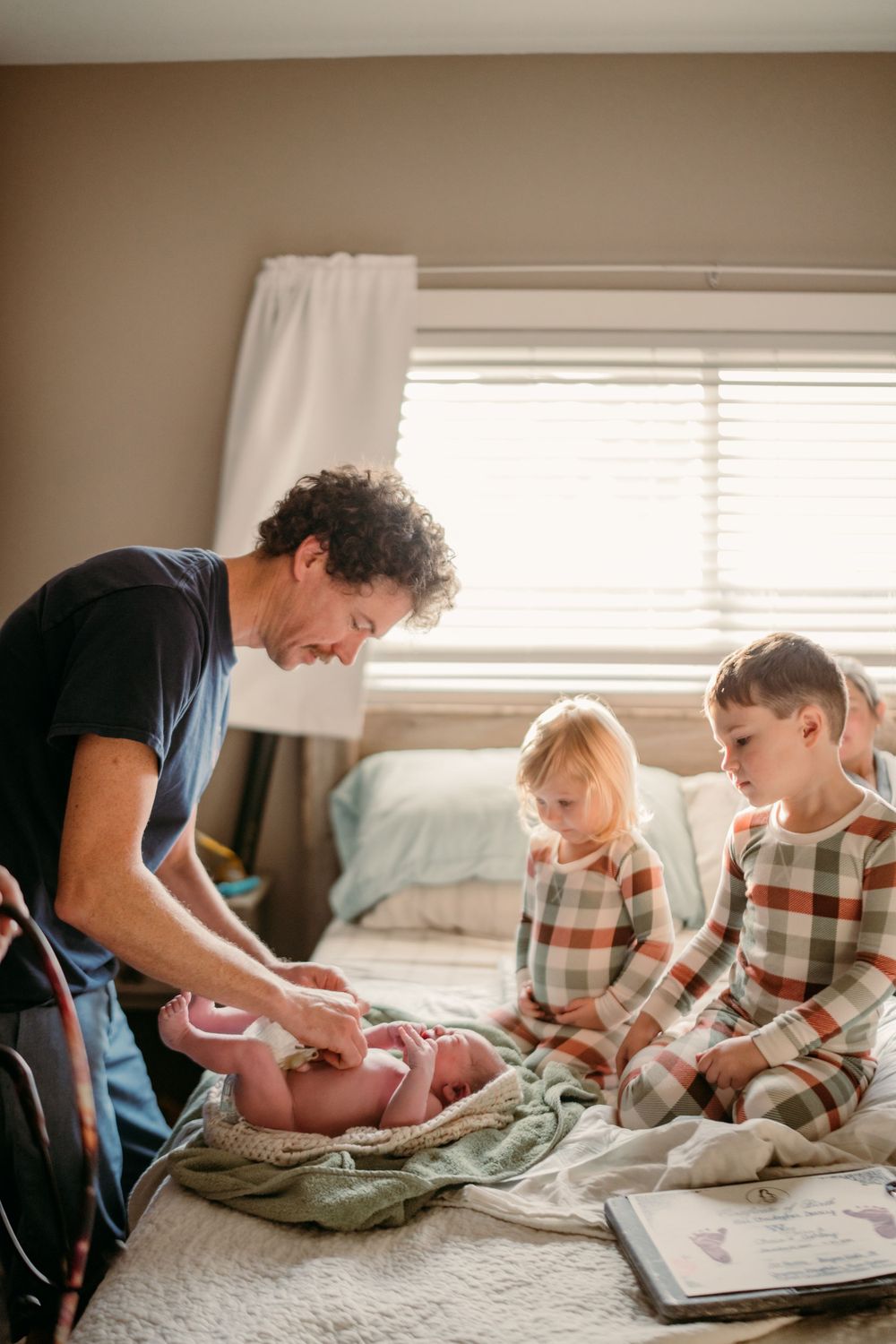 A family spending time together on a bed near a window with natural light streaming in.