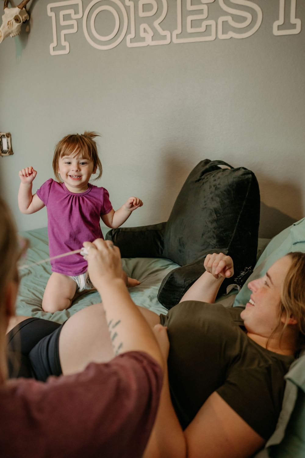 A joyful family moment captured on a bed with a 'Forest' sign visible in the background.