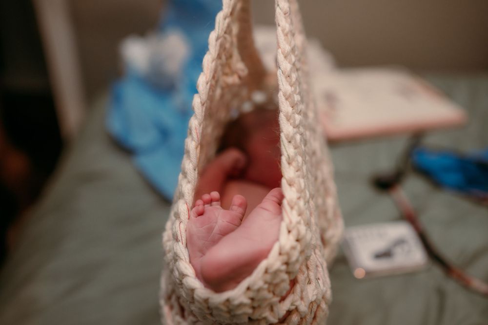 A tiny newborn baby foot nestled in soft crocheted fabric with medical supplies visible in background.