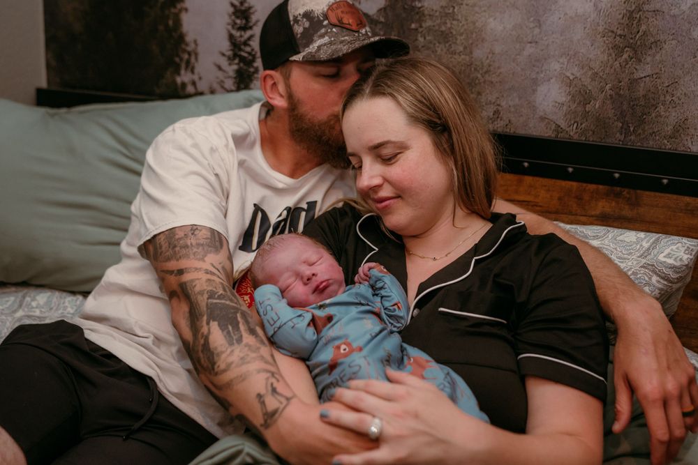A cozy family moment showing parents lovingly holding their newborn baby while resting on a grey couch.