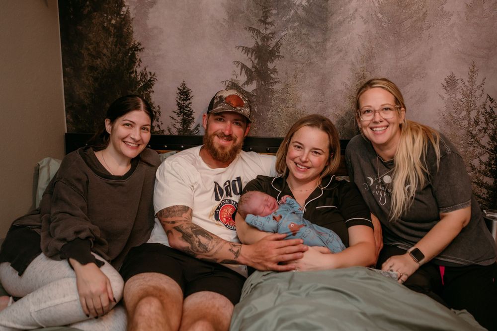 Group sitting together on couch with baby in forest-themed studio setting with textured backdrop.