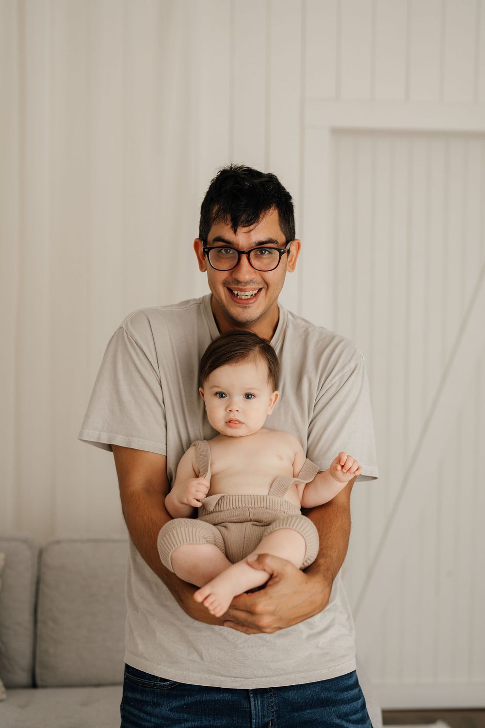 Sweet indoor portrait with baby sitting on lap against grey couch.