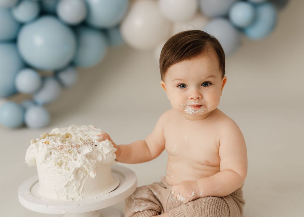 Baby's first cake smash photo session with white cake and blue balloon backdrop.