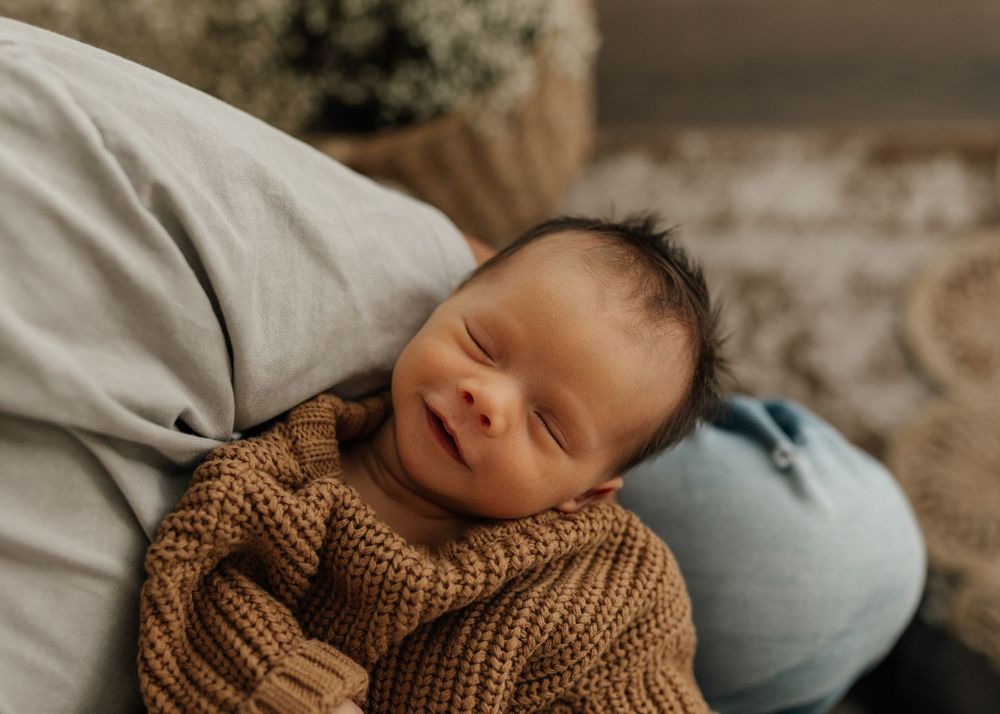 A sleeping newborn baby wearing a cozy brown knit sweater rests peacefully.