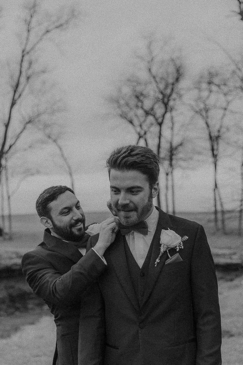 A candid black and white outdoor wedding photo capturing a tender moment between two people in formalwear.