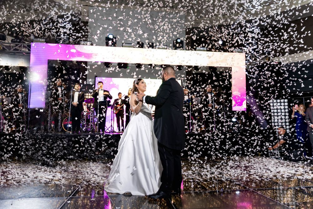 Confetti falls as a couple shares their first dance under purple lighting.
