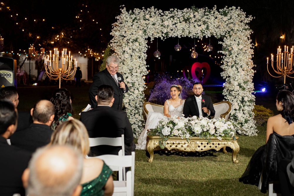 An outdoor wedding ceremony under a beautiful white floral arch with candlelit decorations.