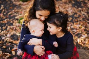 Three people sit together on fallen autumn leaves, wearing navy sweaters while sharing an intimate moment.